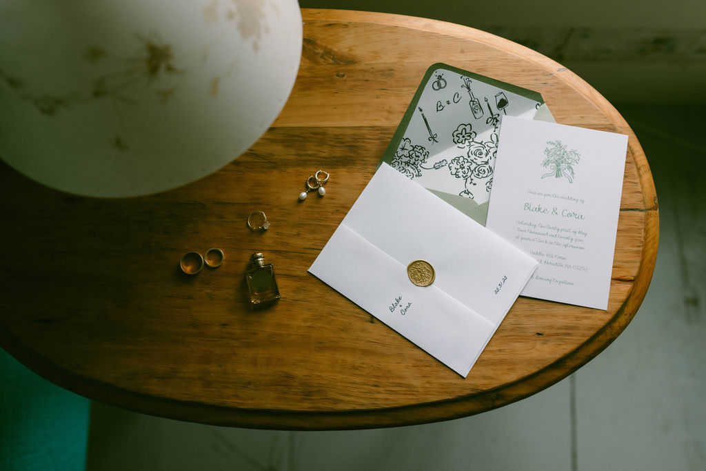 wedding invitations and rings on wood table with lamp Saddle Hill Farm wedding