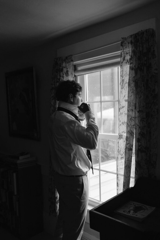 groom getting ready in front of window Saddle Hill Farm wedding