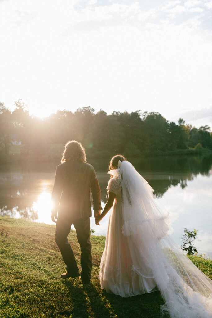 couple holding hands walking through the field with the sun in the background
