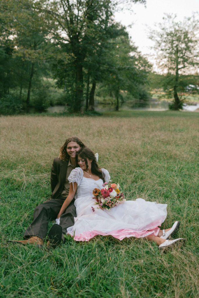 bride and groom sitting in the field before her ceremony 