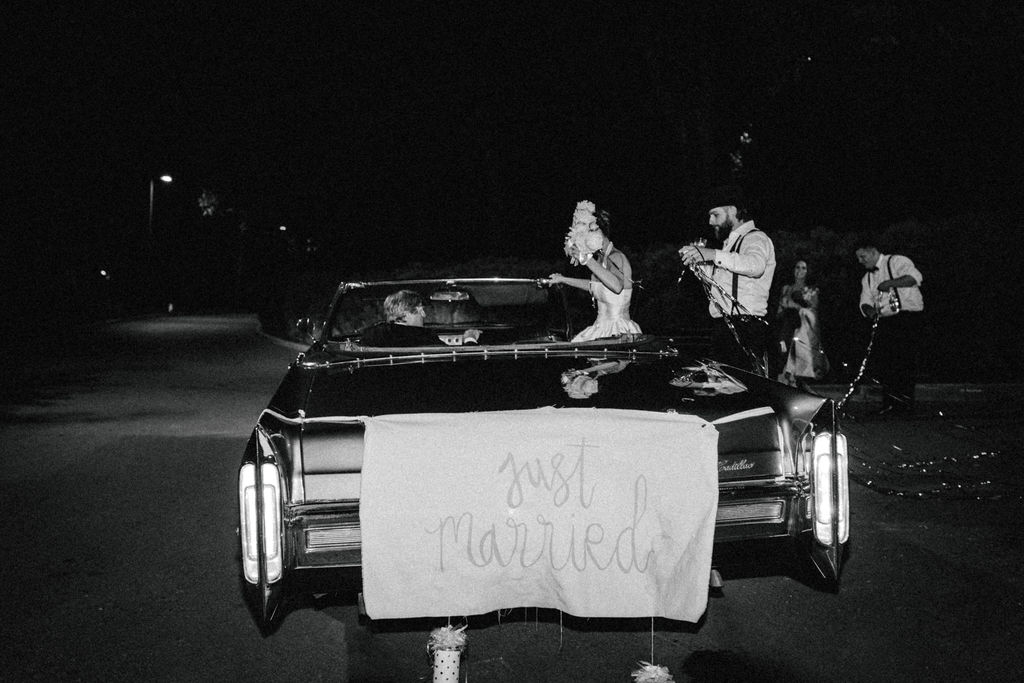 Bride & Groom leaving reception in vintage car with linen hand painted just married sign with cans tied on the back