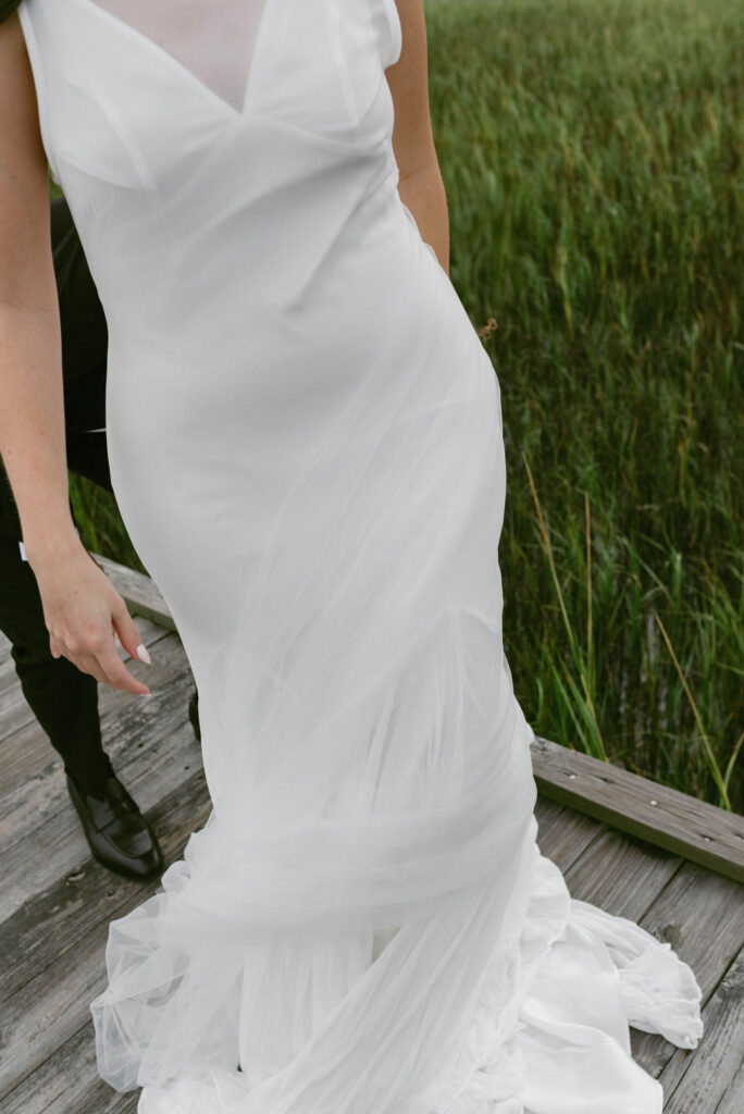 bride's veil wrapped around her on a dock 
