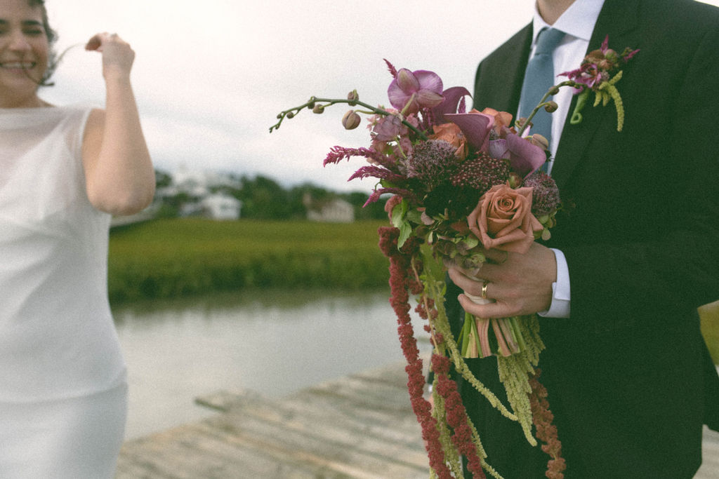 bride and groom on dock. Bride's hair blowing in the wind and groom holding the bouquet 
