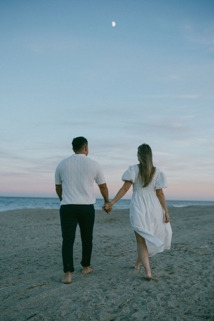 couple walking at the beach during the blue light at their cozy beach engagement session 