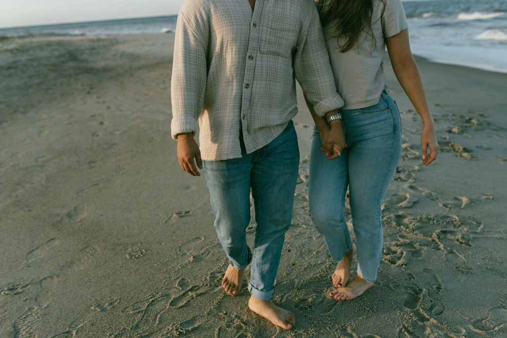 couple holding hands walking on the beach during their cozy beach engagement session