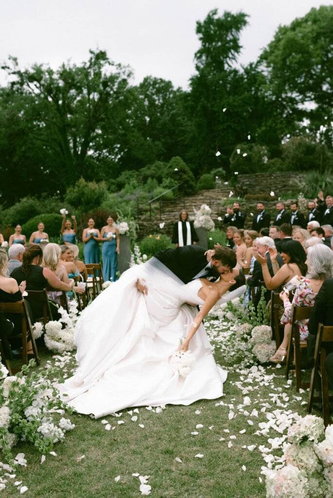 Bride & groom in a dip kiss after getting married walking down the aisle flower confetti toss